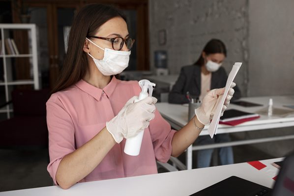 Cleaner spraying disinfectant on office equipment